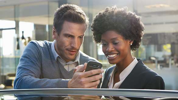 Aplikacje mobilne BMW. Telefon w dłoni męzczyzny, który prezentuje aplikację kobiecie.